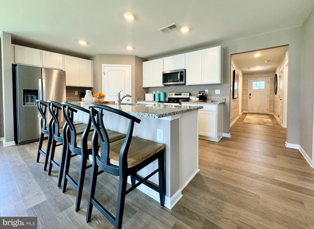 kitchen featuring white cabinets, appliances with stainless steel finishes, light wood-type flooring, and a kitchen island with sink