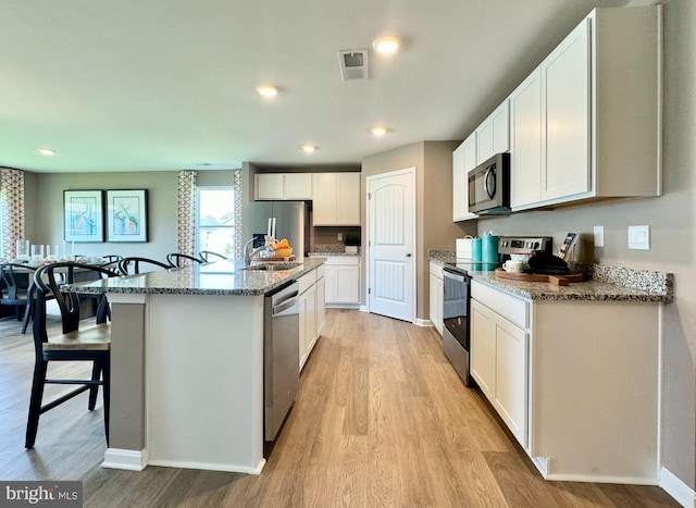 kitchen featuring a kitchen bar, stainless steel appliances, light hardwood / wood-style floors, white cabinetry, and an island with sink