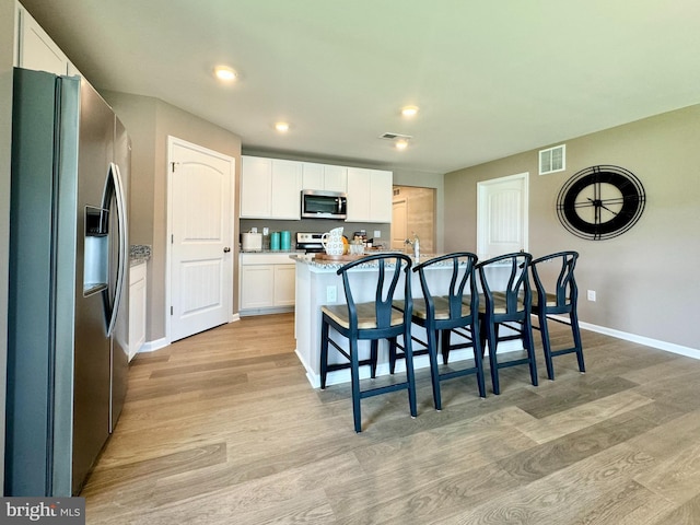 kitchen with light hardwood / wood-style flooring, white cabinetry, appliances with stainless steel finishes, and a kitchen island with sink