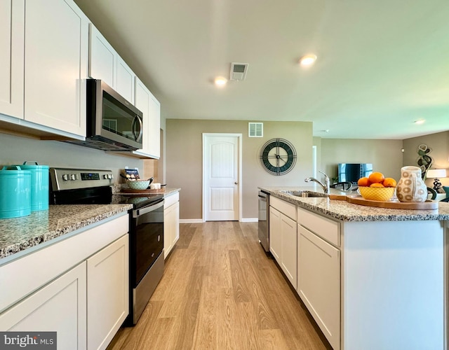 kitchen with light stone counters, white cabinets, light wood-type flooring, and appliances with stainless steel finishes