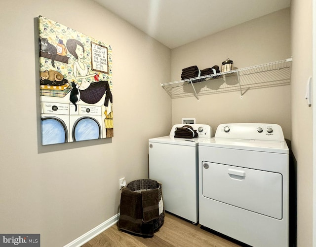 clothes washing area with washing machine and clothes dryer and light wood-type flooring