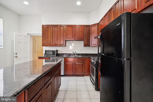 kitchen featuring sink, backsplash, dark stone counters, light tile patterned flooring, and appliances with stainless steel finishes