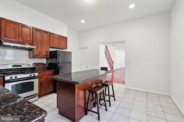 kitchen featuring a center island, stainless steel gas range oven, a breakfast bar area, black refrigerator, and light tile patterned floors