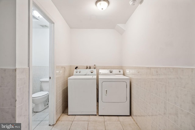 clothes washing area with light tile patterned floors, tile walls, and washing machine and clothes dryer