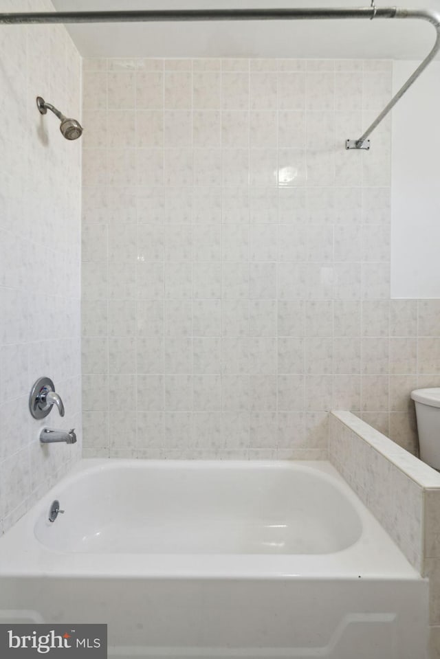 bathroom with toilet, tiled shower / bath, and tile walls