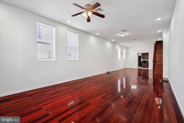 unfurnished living room with ceiling fan with notable chandelier and dark wood-type flooring