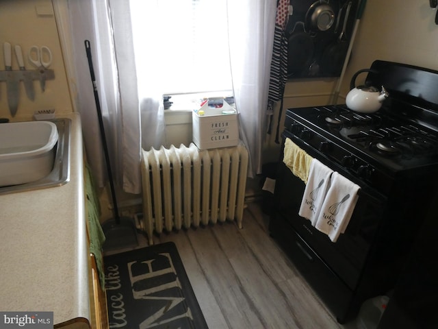 kitchen with hardwood / wood-style flooring, radiator, and black range with gas cooktop