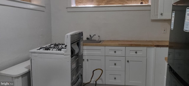 kitchen featuring white cabinets, black fridge, sink, gas range gas stove, and butcher block counters