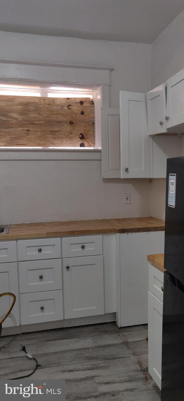 kitchen featuring butcher block counters, light hardwood / wood-style floors, black fridge, and white cabinetry