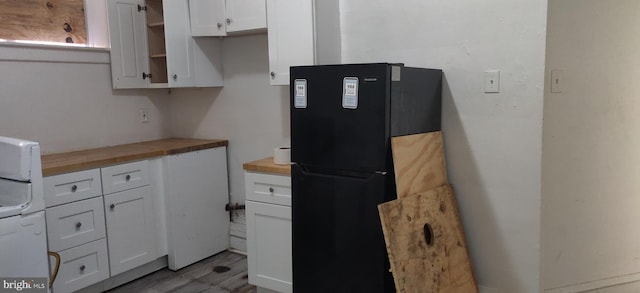 kitchen with butcher block countertops, black fridge, white cabinetry, and light wood-type flooring