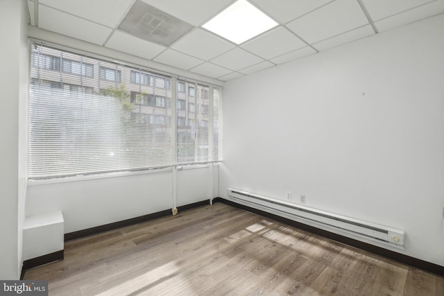 empty room with wood-type flooring, a drop ceiling, and baseboard heating