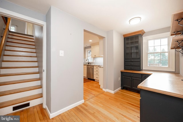 kitchen featuring light wood-type flooring, backsplash, stainless steel dishwasher, gray cabinetry, and sink