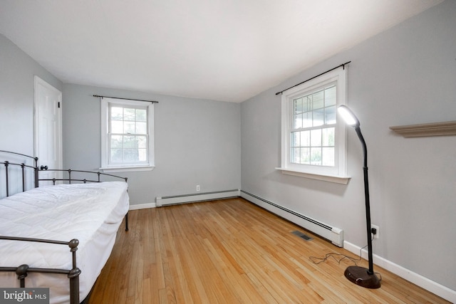 unfurnished bedroom with multiple windows, hardwood / wood-style floors, and a baseboard radiator