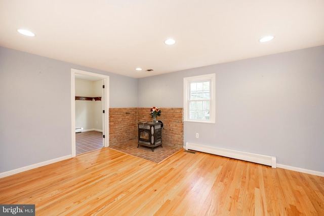 unfurnished living room featuring baseboard heating, a wood stove, and hardwood / wood-style floors