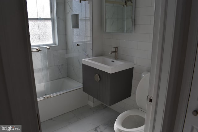 full bathroom with vanity, toilet, tile walls, and bath / shower combo with glass door