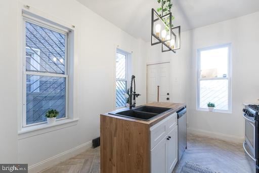 kitchen featuring appliances with stainless steel finishes, sink, decorative light fixtures, white cabinets, and light parquet flooring