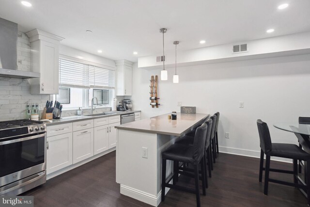 kitchen with a kitchen breakfast bar, white cabinetry, wall chimney range hood, dark wood-type flooring, and stainless steel appliances