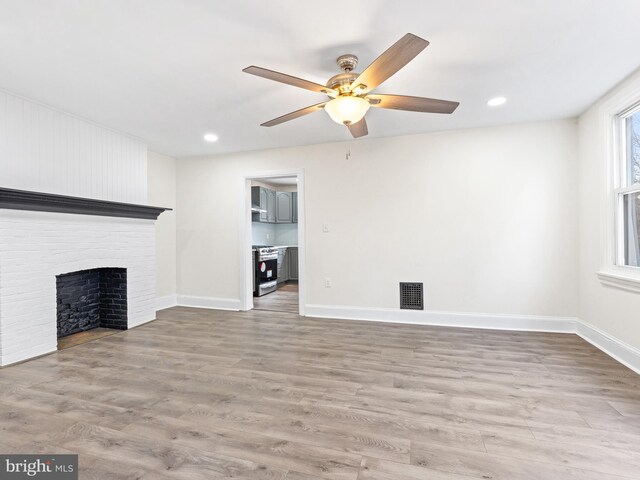 unfurnished living room featuring ceiling fan, light hardwood / wood-style flooring, and a brick fireplace