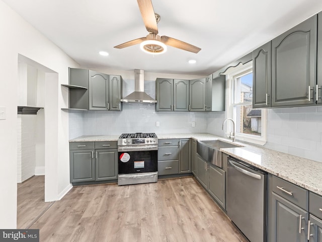 kitchen featuring gray cabinetry, sink, wall chimney range hood, light hardwood / wood-style floors, and appliances with stainless steel finishes