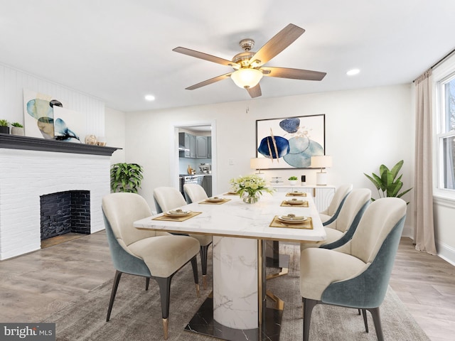 dining area with ceiling fan, wood-type flooring, and a brick fireplace