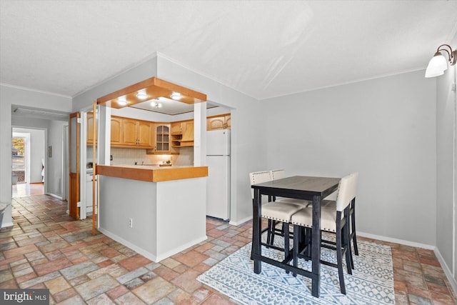 kitchen with kitchen peninsula, light brown cabinetry, backsplash, white refrigerator, and a kitchen breakfast bar