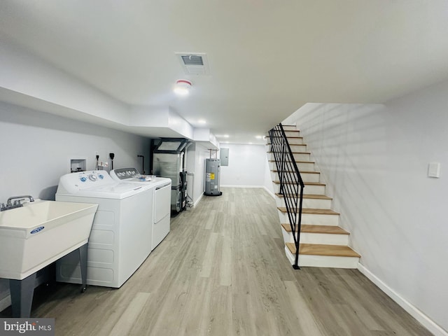 clothes washing area with washing machine and dryer, electric water heater, sink, and light wood-type flooring