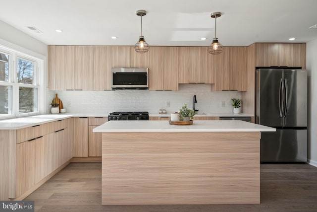 kitchen with appliances with stainless steel finishes, light wood-type flooring, light brown cabinetry, pendant lighting, and a center island