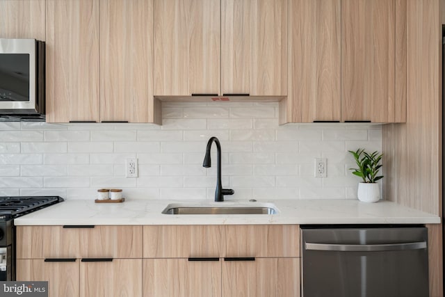 kitchen with light brown cabinetry, stainless steel appliances, light stone counters, and sink