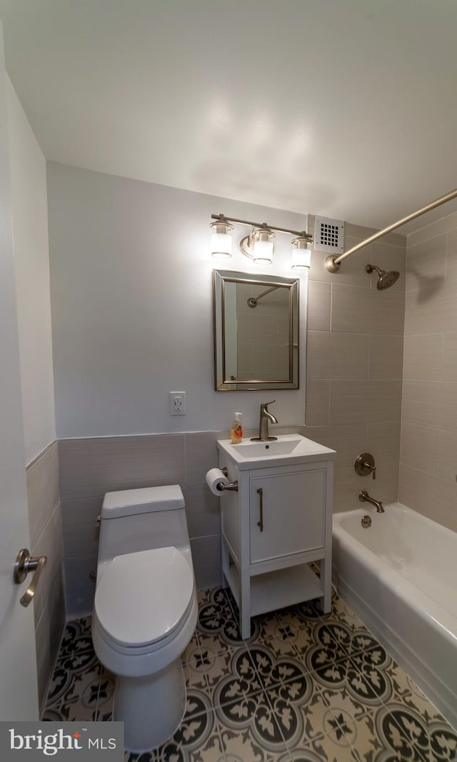 full bathroom with vanity, tile patterned floors, tiled shower / bath combo, toilet, and tile walls