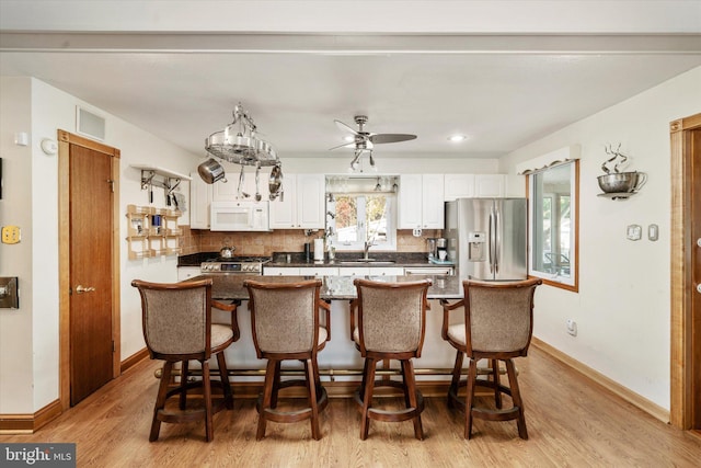 kitchen featuring white cabinets, sink, light wood-type flooring, a kitchen bar, and stainless steel appliances