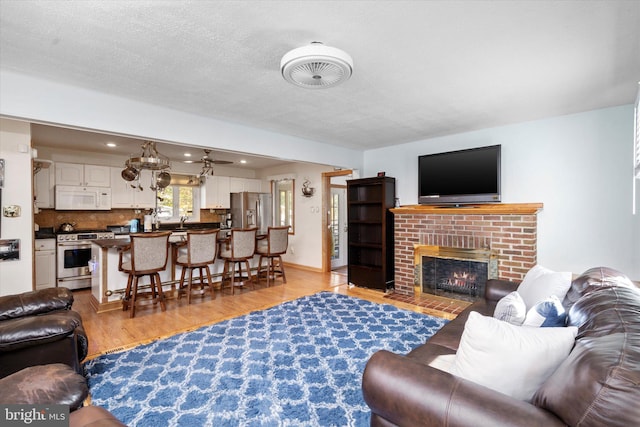 living room featuring a fireplace, a textured ceiling, light hardwood / wood-style flooring, and ceiling fan