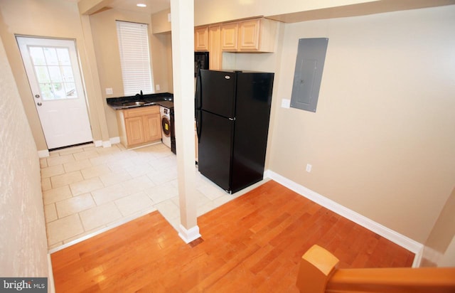 kitchen featuring black refrigerator, light brown cabinetry, sink, light hardwood / wood-style flooring, and washer / clothes dryer