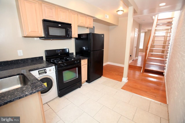 kitchen featuring sink, light hardwood / wood-style flooring, washer / clothes dryer, dark stone countertops, and black appliances