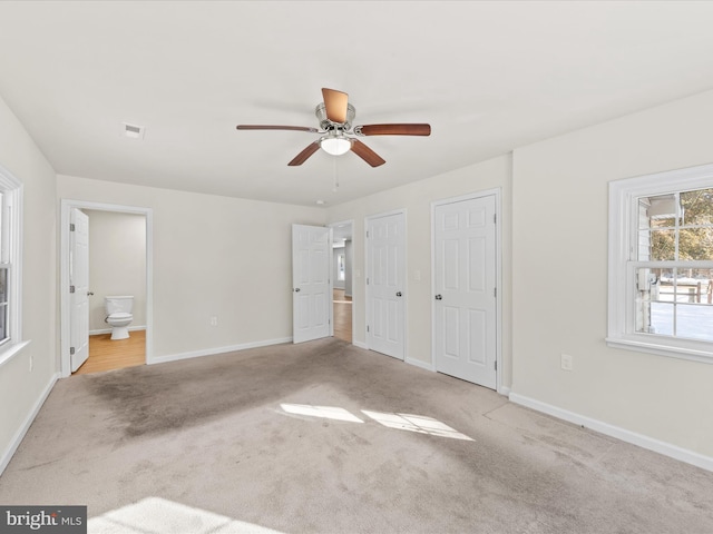 unfurnished bedroom featuring connected bathroom, two closets, ceiling fan, and light colored carpet