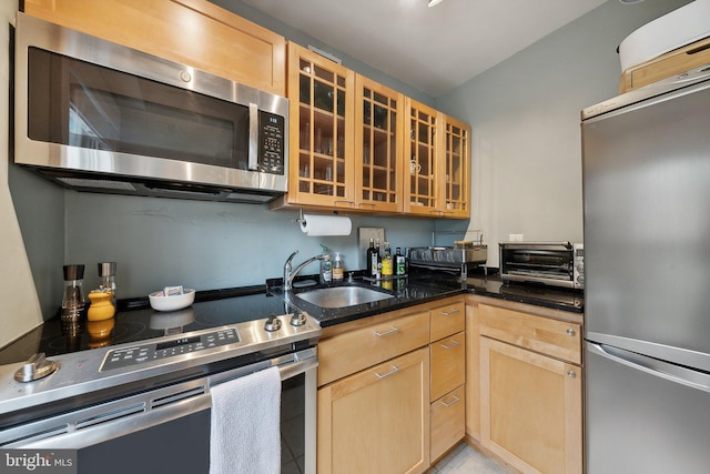 kitchen with appliances with stainless steel finishes, light brown cabinets, dark stone countertops, and sink