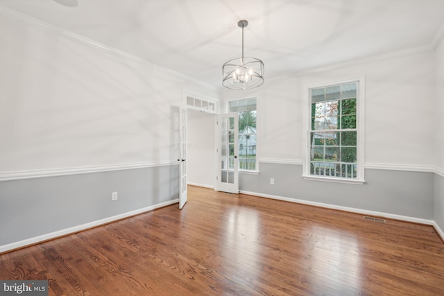 spare room featuring wood-type flooring, crown molding, and an inviting chandelier