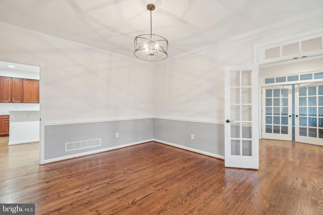 spare room with hardwood / wood-style flooring, a notable chandelier, crown molding, and french doors