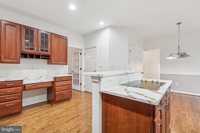 kitchen with decorative backsplash, black electric stovetop, light stone counters, pendant lighting, and light hardwood / wood-style floors