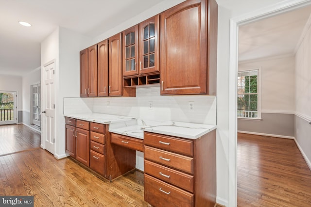 kitchen with light wood-type flooring, light stone counters, plenty of natural light, and backsplash