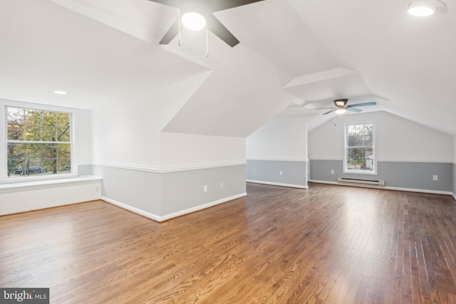 additional living space featuring hardwood / wood-style floors, ceiling fan, a healthy amount of sunlight, and baseboard heating