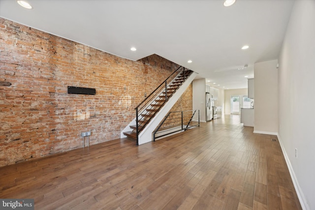 unfurnished living room featuring brick wall and hardwood / wood-style flooring