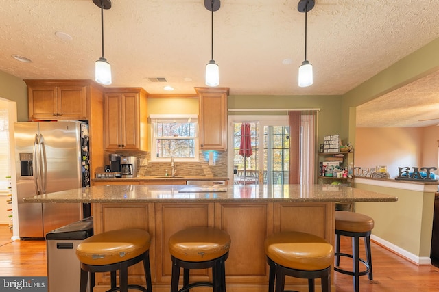 kitchen with stainless steel fridge, light wood-type flooring, and hanging light fixtures