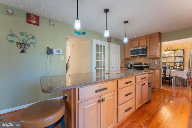 kitchen with appliances with stainless steel finishes, light wood-type flooring, a center island, and pendant lighting