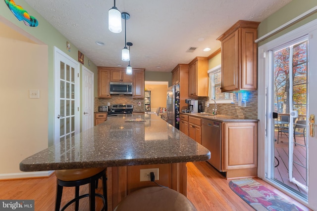 kitchen with decorative backsplash, dark stone counters, stainless steel appliances, decorative light fixtures, and light hardwood / wood-style floors