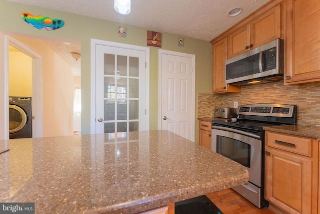 kitchen with a textured ceiling, stone counters, stainless steel appliances, and washer / clothes dryer