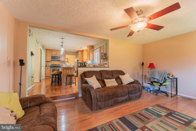 living room featuring ceiling fan, light hardwood / wood-style floors, and a textured ceiling