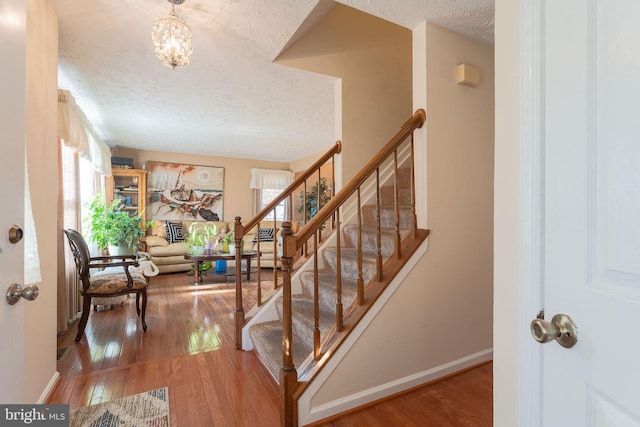 stairway with an inviting chandelier, a textured ceiling, and hardwood / wood-style flooring