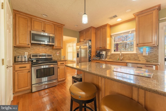 kitchen with sink, stainless steel appliances, dark stone counters, light hardwood / wood-style floors, and a breakfast bar