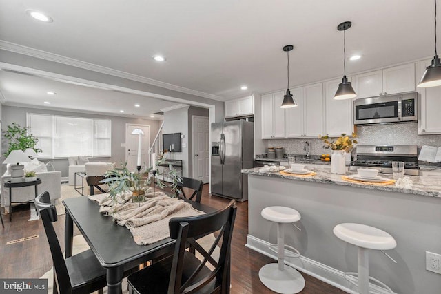 kitchen with pendant lighting, dark wood-type flooring, white cabinets, light stone countertops, and appliances with stainless steel finishes