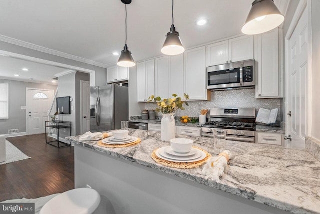 kitchen featuring white cabinets, light stone countertops, ornamental molding, appliances with stainless steel finishes, and dark hardwood / wood-style flooring